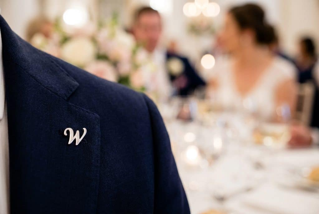 _close-up-of-lapel-pin-with-blurred-wedding-reception._