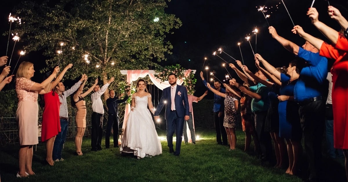 Bride and groom walking through a tunnel of sparklers at night as guests hold them high on both sides