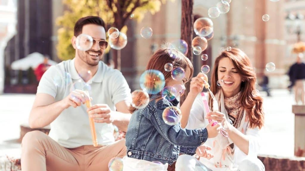 Family blowing bubbles together outdoors on a sunny day in a town square