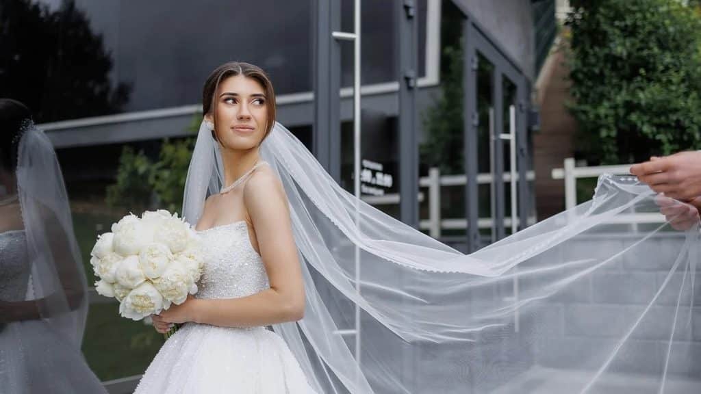 Bride holding white peonies as her long cathedral veil billows out behind her