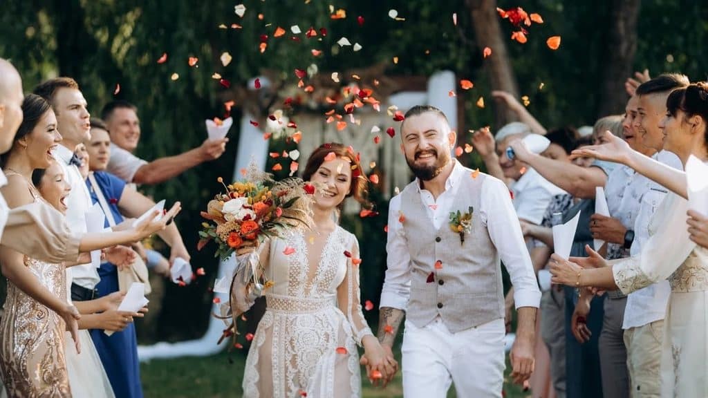 Guests tossing petals from paper cones over a laughing couple during a daytime wedding exit