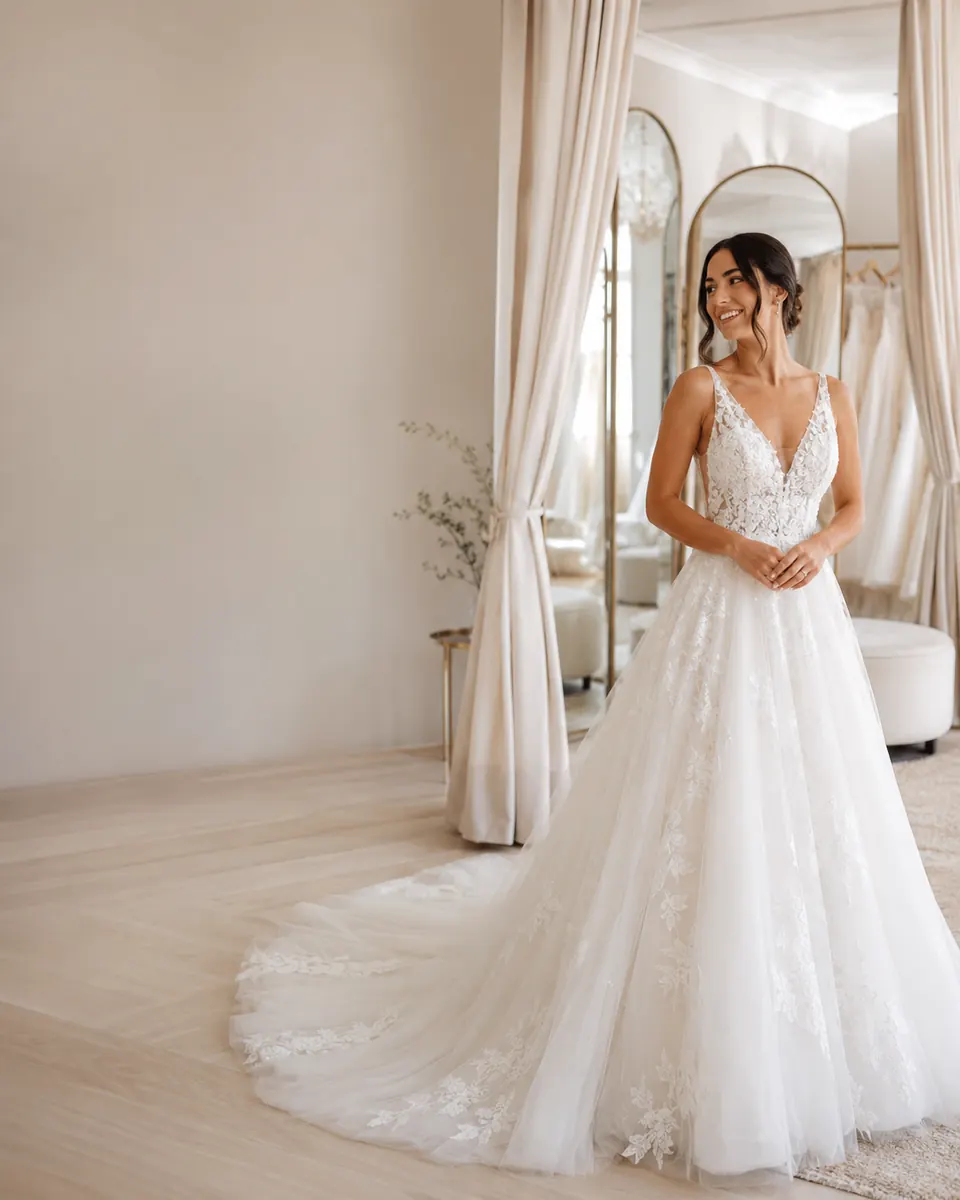 Bride smiling while a consultant helps adjust her wedding dress during a fitting